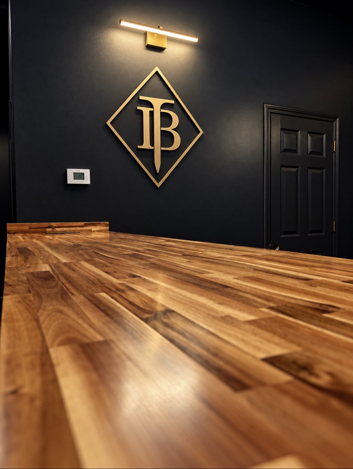 Gold Black Tee diamond logo lit on a dark wall above a long wooden counter